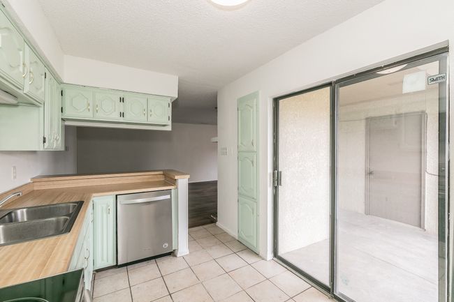 Kitchen with dishwasher, green cabinetry, a sink, light tile patterned floors, and butcher block countertops | Image 9