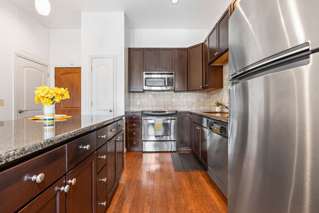 Kitchen with appliances with stainless steel finishes, dark stone countertops, dark wood-style flooring, a sink, and dark brown cabinetry | Image 4