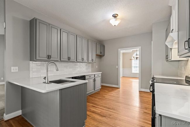Kitchen with gray cabinetry, black range with electric stovetop, a peninsula, a sink, and backsplash | Image 14