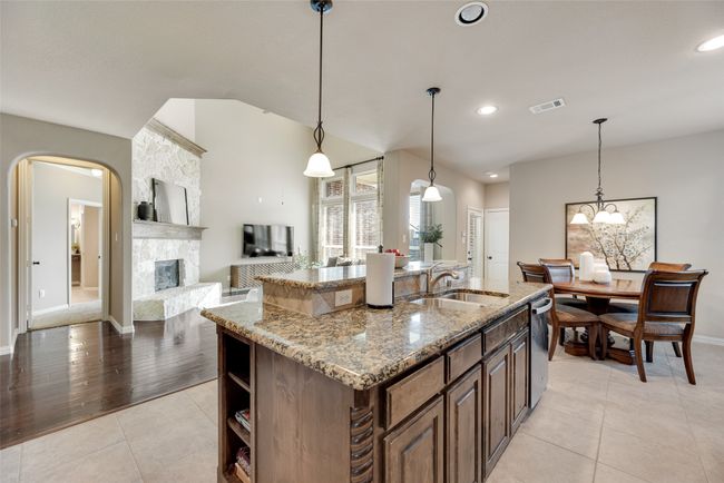 Kitchen featuring light stone countertops, an island with sink, light tile patterned floors, dishwasher, and decorative light fixtures | Image 6
