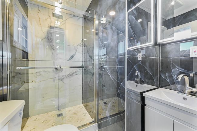 Bathroom with toilet, tile walls, vanity, a shower with door, and decorative backsplash | Image 31