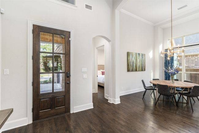Elegant and radiant, this grand entryway is awash in natural light, showcasing exquisite upgrades such as hand-scraped hardwood floors, a custom glass-inlay front door, and designer light fixtures that elevate the space with timeless sophistication. | Image 5