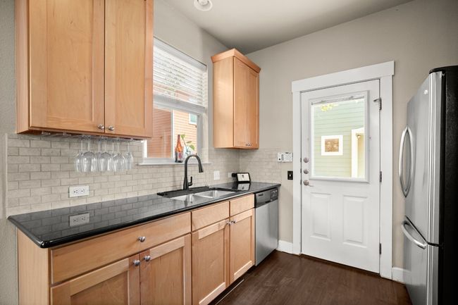 Kitchen featuring light brown cabinets, dark wood-type flooring, decorative backsplash, stainless steel appliances, and a sink | Image 11