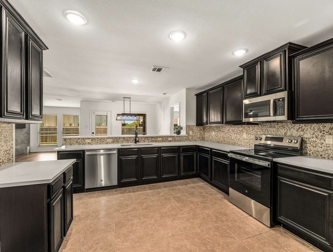 Kitchen with appliances with stainless steel finishes, dark cabinets, tasteful backsplash, light countertops, and a peninsula | Image 15