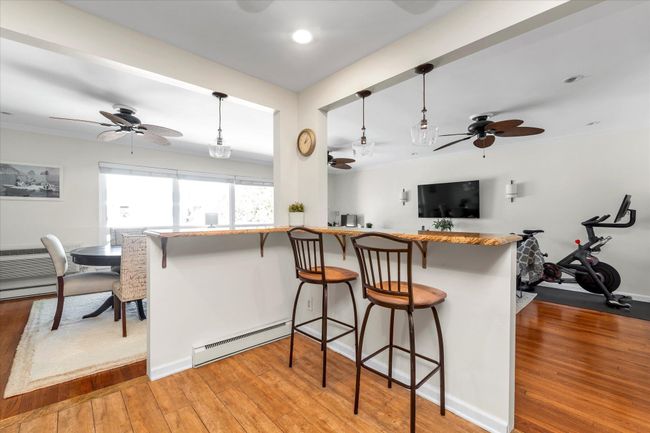 Kitchen featuring light wood-style flooring, a ceiling fan, a breakfast bar area, and a baseboard heating unit | Image 6