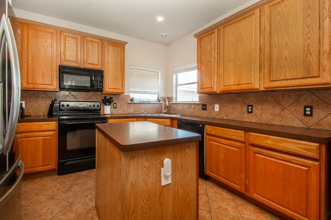 Kitchen featuring black appliances, a sink, dark countertops, a kitchen island, and recessed lighting | Image 6