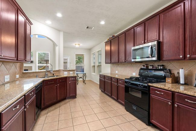 Spacious kitchen with rich wood cabinetry, granite countertops, and modern appliances. Features a gas range, ample storage, and a bright, open layout with tiled flooring. Ideal for cooking and entertaining. | Image 8