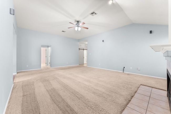 Unfurnished living room with a ceiling fan, visible vents, a fireplace, vaulted ceiling, and carpet floors | Image 8