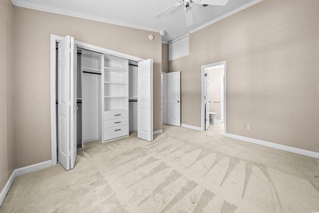 Unfurnished bedroom featuring ceiling fan, light carpet, baseboards, ensuite bathroom, and ornamental molding | Image 12