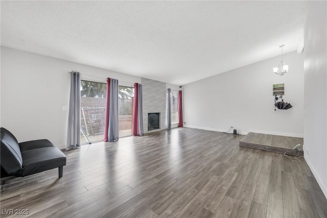 Living room with baseboards, wood finished floors, a chandelier, and a fireplace | Image 10