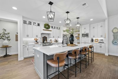 A chef’s kitchen awaits with its massive granite-topped center island, stainless steel appliances, and herringbone tile backsplash that pairs beautifully with custom shaker cabinetry | Image 3