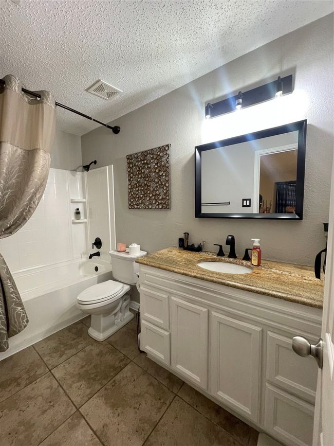 Full bath featuring a textured ceiling, vanity, shower / bath combo with shower curtain, and tile patterned floors | Image 17