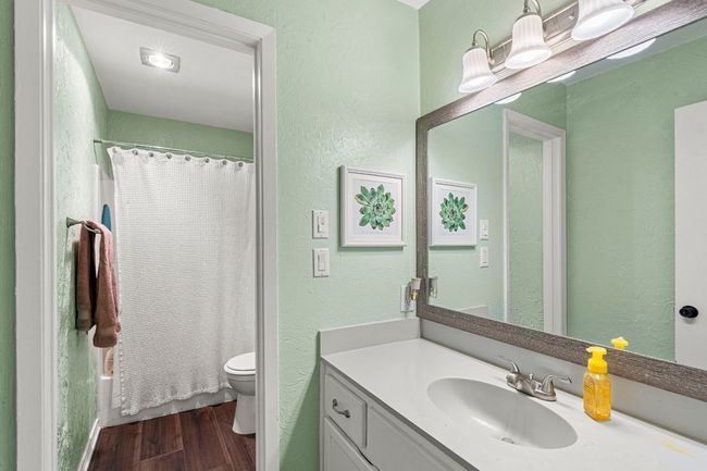 Full bath with vanity, wood finished floors, toilet, a textured wall, and shower / bathtub combination with curtain | Image 16