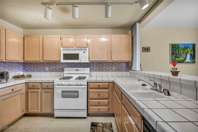 Kitchen with light brown cabinetry, tile countertops, a sink, white appliances, and tasteful backsplash | Image 34