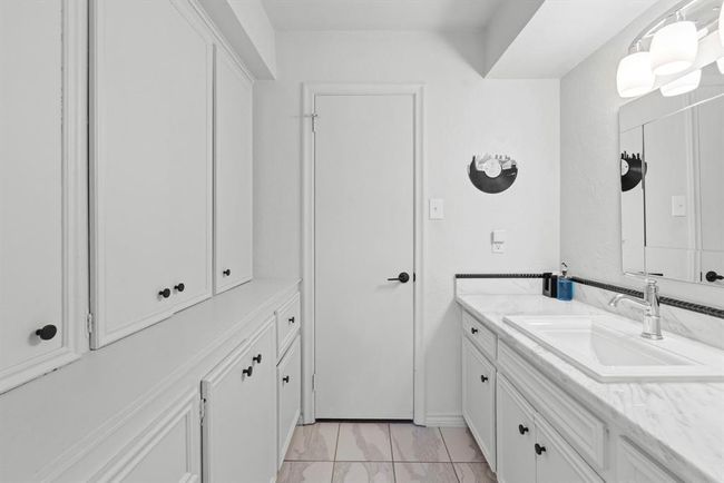 This bathroom features a clean, white design with ample cabinetry for storage, a large mirror, and modern lighting. The countertop is sleek with a single sink, offering a functional and stylish space. | Image 27