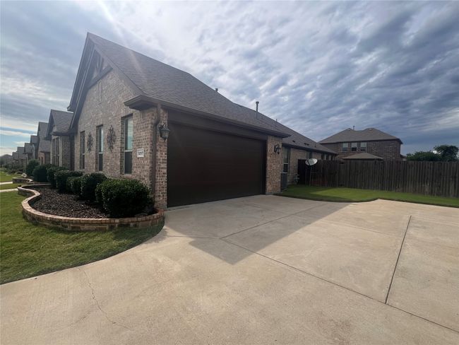 View of property exterior featuring brick siding, driveway, a garage, and a shingled roof | Image 5