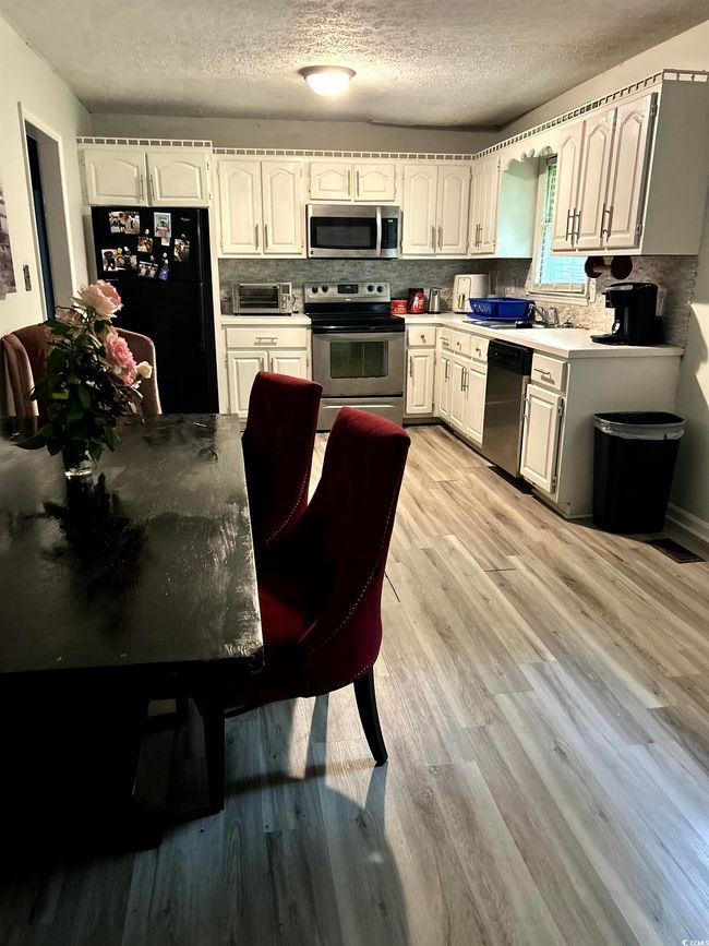 Kitchen with stainless steel appliances, light wood finished floors, a textured ceiling, backsplash, and white cabinetry | Image 13