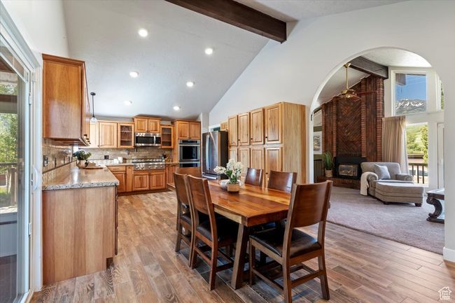 Dining room featuring beamed ceiling, arched walkways, high vaulted ceiling, a fireplace, and light wood-type flooring | Image 5