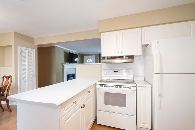 Kitchen with white appliances, range hood, light countertops, and a peninsula | Image 15