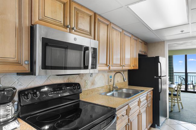 Kitchen with black appliances, a sink, light countertops, decorative backsplash, and light tile patterned floors | Image 14