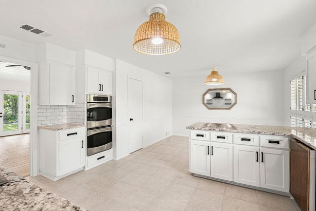 Kitchen with double oven, white cabinets, a peninsula, decorative backsplash, and light stone counters | Image 11