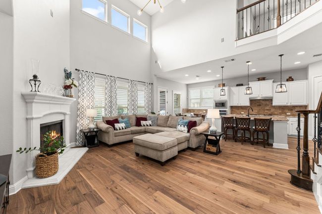 Soaring two-story ceilings, a wall of windows for abundant natural light, and a striking wood-burning fireplace create a dramatic centerpiece in this open-concept living area. Beautiful hardwood floors and open sightlines to the kitchen and dining spaces make it ideal for both everyday living and entertaining. | Image 6
