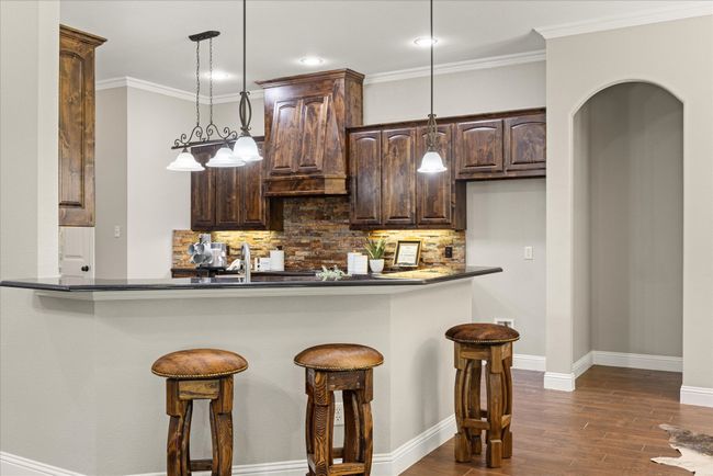 Kitchen with dark brown cabinetry, dark countertops, tasteful backsplash, a kitchen bar, and dark wood-style floors | Image 15