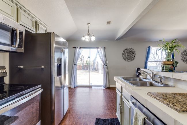 Kitchen with appliances with stainless steel finishes, sink, cream cabinets, a notable chandelier, and hanging light fixtures | Image 7