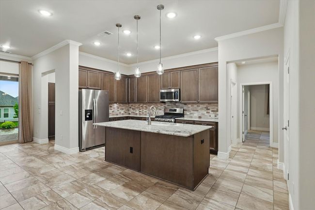 Kitchen featuring appliances with stainless steel finishes, decorative backsplash, dark brown cabinets, crown molding, and a kitchen island with space for barstools | Image 4