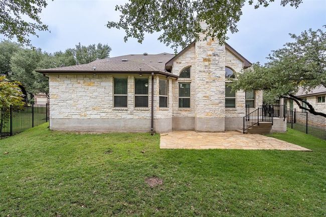 Rear view of house with stone siding, a fenced backyard, a patio, and roof with shingles | Image 21