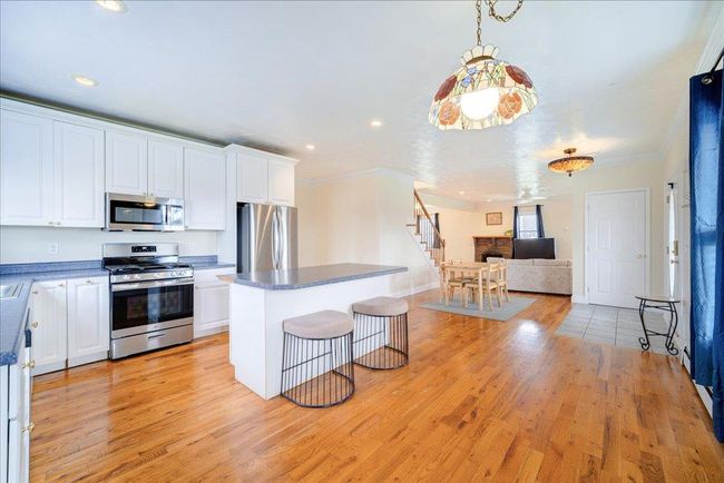 Kitchen with light wood-style floors, ornamental molding, white cabinets, appliances with stainless steel finishes, and open floor plan | Image 14