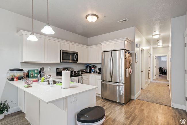 Kitchen featuring stainless steel appliances, a peninsula, white cabinets, light wood-style floors, and light countertops | Image 4
