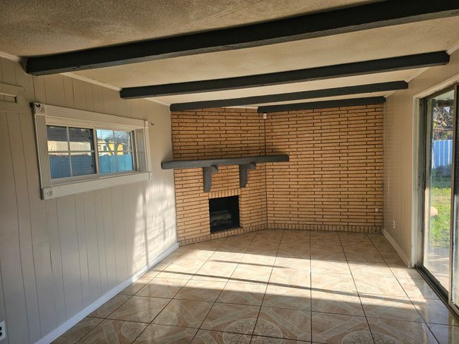 Unfurnished living room with beam ceiling, a textured ceiling, brick wall, wood walls, and a brick fireplace | Image 23