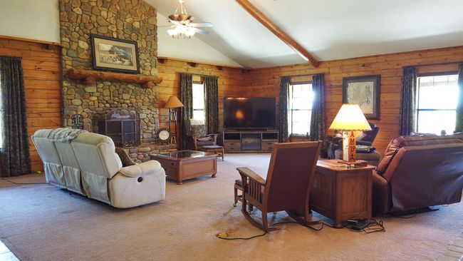 Carpeted living room with wooden walls, a fireplace, and a wealth of natural light | Image 9