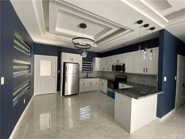Kitchen featuring stainless steel appliances, a tray ceiling, a peninsula, tasteful backsplash, and white cabinets | Image 5