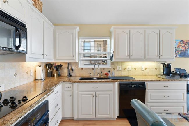 This kitchen features granite countertops, white cabinetry, and a tiled backsplash. It includes modern appliances, under-cabinet lighting, and ample storage, creating a functional and inviting cooking space. | Image 19