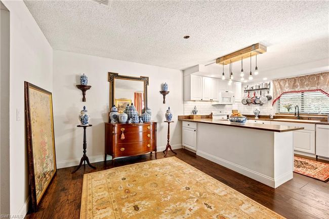 Kitchen with dark wood-type flooring, white cabinets, a textured ceiling, tasteful backsplash, and a peninsula | Image 15