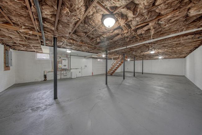 Unfinished basement with tankless water heater, concrete block wall, stairs, and electric panel | Image 28