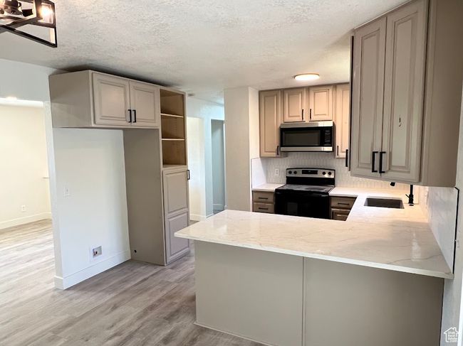 Kitchen featuring electric stove, stainless steel microwave, a peninsula, light stone countertops, and light wood-type flooring | Image 4