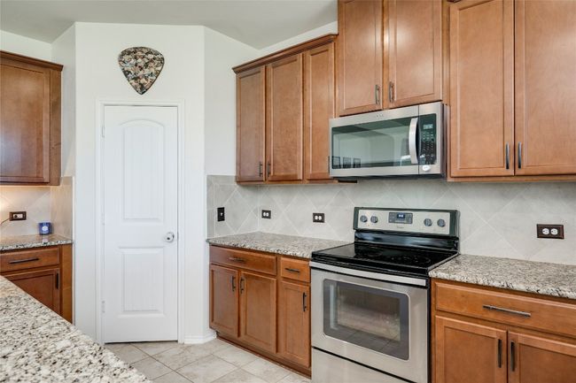 Kitchen featuring stainless steel appliances, brown cabinets, light stone countertops, and backsplash | Image 9