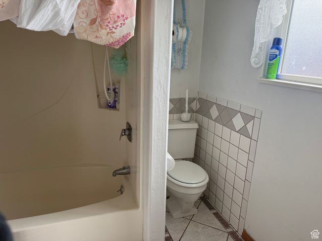 Full bathroom featuring toilet, tile patterned flooring, shower combination, and tile walls | Image 15
