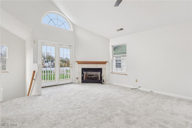 Living room featuring vaulted ceiling, a ceiling fan, a tile fireplace, carpet, Glass Doors leading to balcony | Image 5