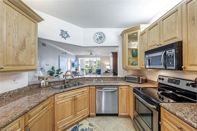 Kitchen featuring appliances with stainless steel finishes, dark stone countertops, a ceiling fan, light tile patterned flooring, and crown molding | Image 4
