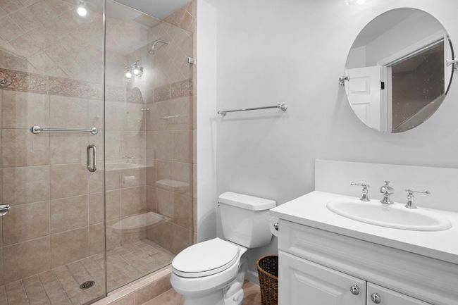 The lower-level full bath offers a spacious glass-enclosed shower, elegant tilework, and a crisp, modern vanity—perfect for guests or post-workout refresh. | Image 35