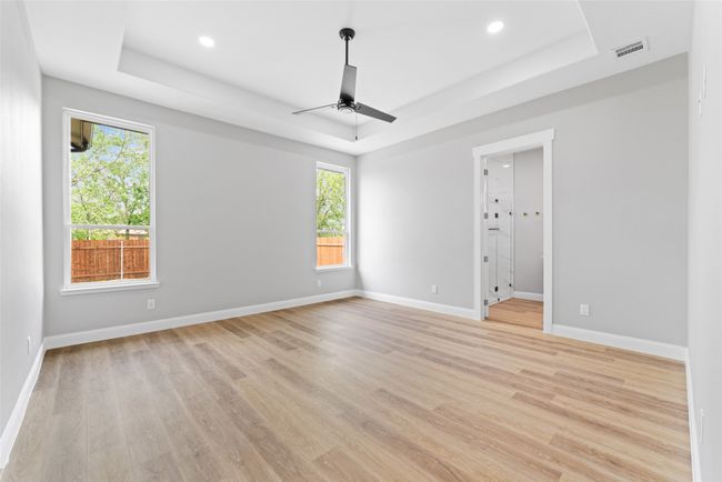 Empty room with a ceiling fan, a tray ceiling, visible vents, and light wood-style floors | Image 21