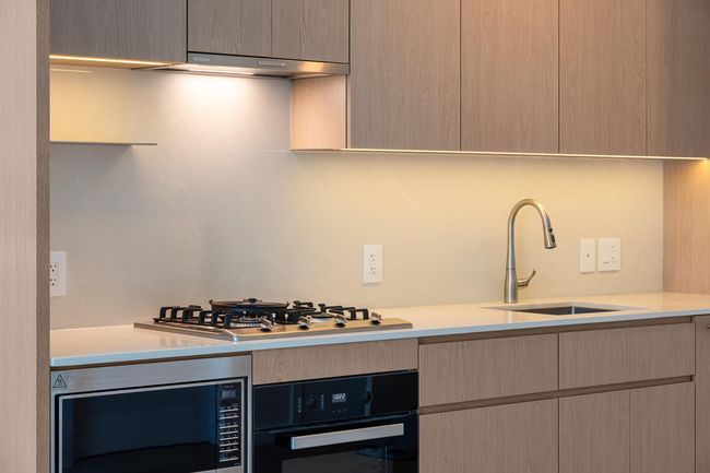 Kitchen with stainless steel appliances, under cabinet range hood, light countertops, and light brown cabinets | Image 16