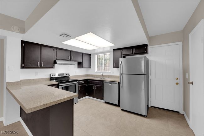 Kitchen featuring appliances with stainless steel finishes, a sink, under cabinet range hood, a peninsula, and light countertops | Image 7