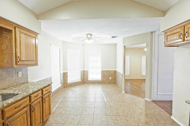 Kitchen with light stone countertops, a ceiling fan, lofted ceiling, open floor plan, and light tile patterned floors | Image 13