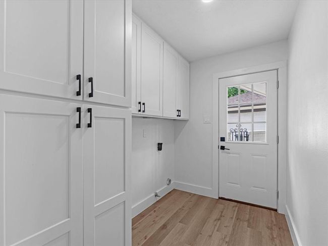 This photo shows a bright laundry room or mudroom with white cabinetry, wood flooring, and a door leading outside. The space is clean, modern, and functional with ample storage. | Image 34
