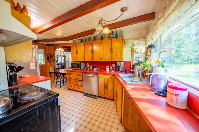 Kitchen featuring stainless steel appliances, light flooring, under cabinet range hood, wooden ceiling, and brown cabinetry | Image 6